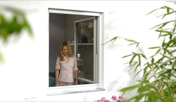Frau steht am Fenster und bedient das Insektenschutzrollo