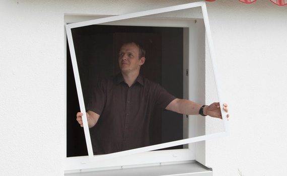 Mann steht innen am Fenster und hält einen Mückengitterrahmen in der Hand