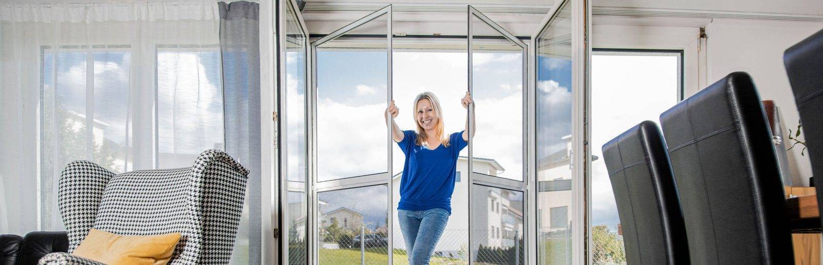 Sara Bachmann steht in einer halb geöffneten Fliegengitter Pendeltür mit 2 Flügeln und hält die Flügel in der Mitte fest
